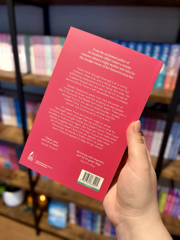 A hand holding the back of a copy of 'A Study in Sparkling' by Jodi McAlister with a hot pink background and white text.