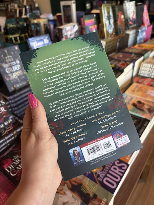 A hand with pink nail polish holding the back cover of 'A Vow Made Twice' featuring a forest and white text.
