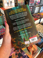A hand with pink nail polish holdsthe back cover of 'Big Bad Wolf' by Laurie Gilmore in a bookstore with blurry books in the background. The cover features a forest scene with white and yellow text for the blurb.