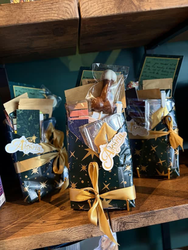 Three mystery books wrapped in green and gold wrapping paper and tied with a gold bow. In the top of the wrapping, there is a selection of accessories.