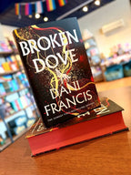 A small stack of the hardcover edition of 'Broken Dove' by Dani Francis, featuring a white wolf in between large, white text and gold and red detailing and matching sprayed edges.