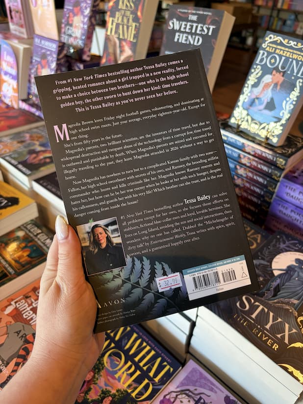A hand with nude nail polish holding the back of a copy of 'Broken Rival' by Tessa Bailey, featuring white and pastel pink text on a dark background.