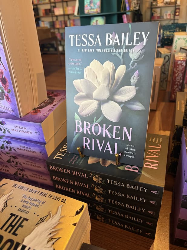 A stack of 'Broken Rival' by Tessa Bailey, featuring a white flower on a dark background, and large text.