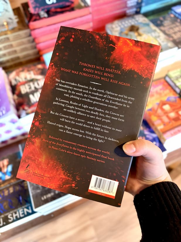 A hand holding the back of a copy of 'Burn of the Everflame' by Penn Cole, featuring a dramatic red and black fiery illustration and white and red text.