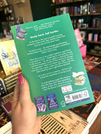 A hand with pink nail polish holding the back of a copy of 'But I Hate Him' by Page Powars with a green background, an illustration of ice skates and a stack of books, and white text.