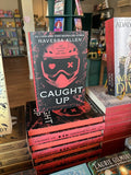 A stack of hardcover copies of 'Caught Up' by Navessa Allen with a single copy standing on top, featuring a red helmet design and red and white text on a dark background.