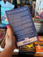 A hand holds the back cover of 'Chase Me if You Can' by Heather Frances, featuring a blue background with white font for the blurb. The book is held in front of a bookstore full of other blurry books in the background. 