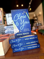 A stack of 'Close to You' by Nissa Renzo, featuring a textured dark blue background with large light blue script title text, a green pencil, pencil shavings, and school-themed paper accents.