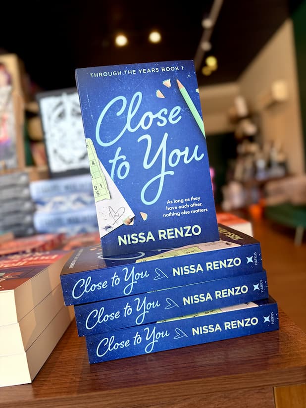 A stack of 'Close to You' by Nissa Renzo, featuring a textured dark blue background with large light blue script title text, a green pencil, pencil shavings, and school-themed paper accents.