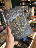 A hand with pink nail polish holding a coy of 'The Shadow Bound Queen: Court of Monsters and Malice' by Eliza Raine with a gold axe, black snakes and gold roses on a dark background.
