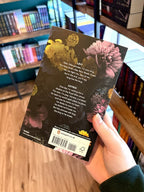 A hand holding the back of a paperback copy of 'Cruel King' by Rina Kent, featuring a dark floral background with yellow, pink, purple, and blue flowers, and white text.
