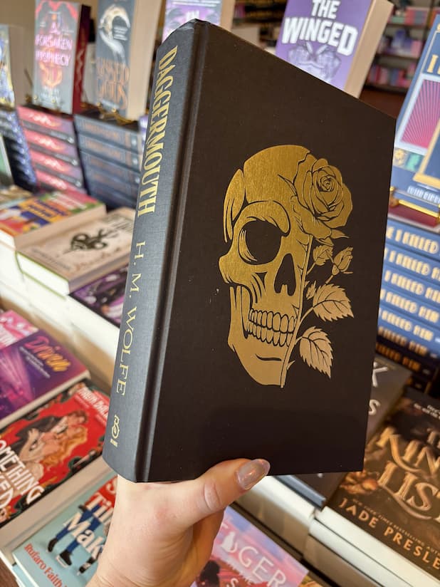 The hardcover book 'Daggermouth' by H. M without the dust jacket, reavling a black book with a gold skull and gold text.