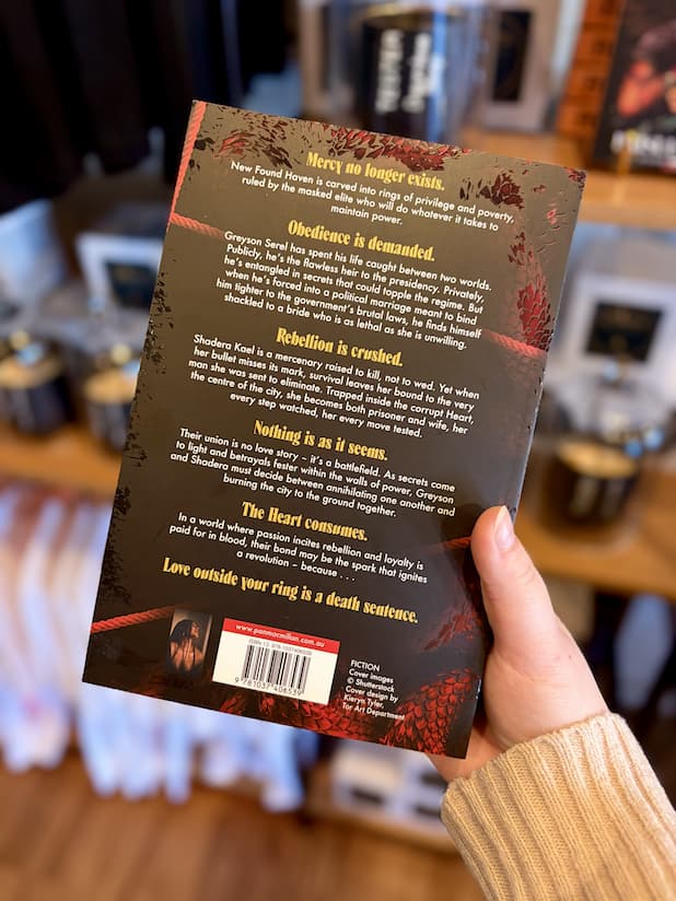 A hand holding the back of a paperback copy of 'Daggermouth' by H. M, featuring a black and red background with white and yellow text.