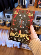 A hand holding a paperback copy of 'Daggermouth' by H. M, featuring a black and red background with a black skull in the centre.