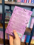 A hand holding the back of a copy of 'Darlin' by Samantha Leigh, featuring a purple background with a floral border and black text.