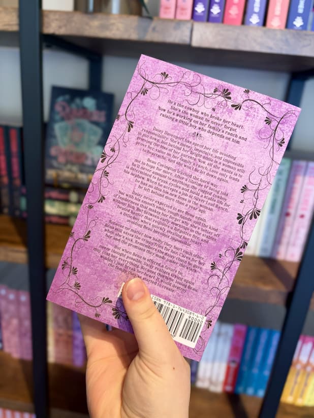 A hand holding the back of a copy of 'Darlin' by Samantha Leigh, featuring a purple background with a floral border and black text.
