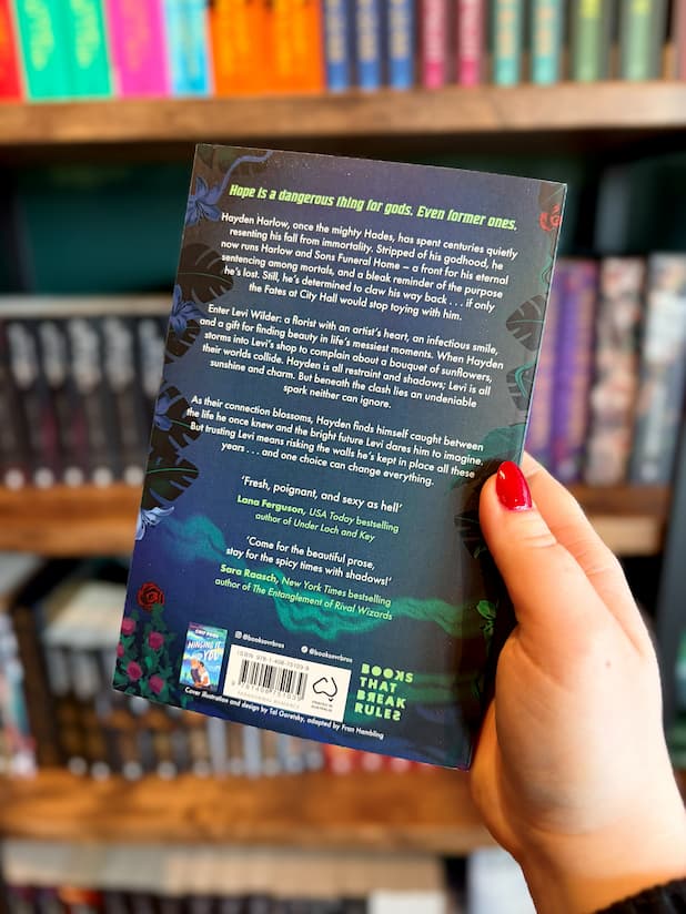 A hand with red nail polish holds the back cover of Dearly Departed by Chip Pons with a blurb of the book and featured comments from USA Today Bestselling author Lana Feguson and New York Times Bestselling author Sara Roasch