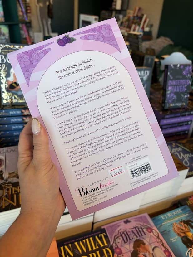 A hand with nude holding the back of a copy of 'Death' by Kristin Cast, featuring a pastel purple background surrounded by floral elements and purple text.