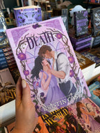 A hand with nude holding a copy of 'Death' by Kristin Cast, featuring a romantic illustration of two characters looking deeply into each other's eyes, he is cradling her face between his hands and they are surrounded by floral elements.