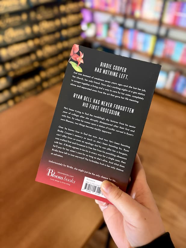 A hand holding the back of a paperback copy of 'Devil' by Sierra Simone, featuring a black background that fades to red at the bottom and white text.