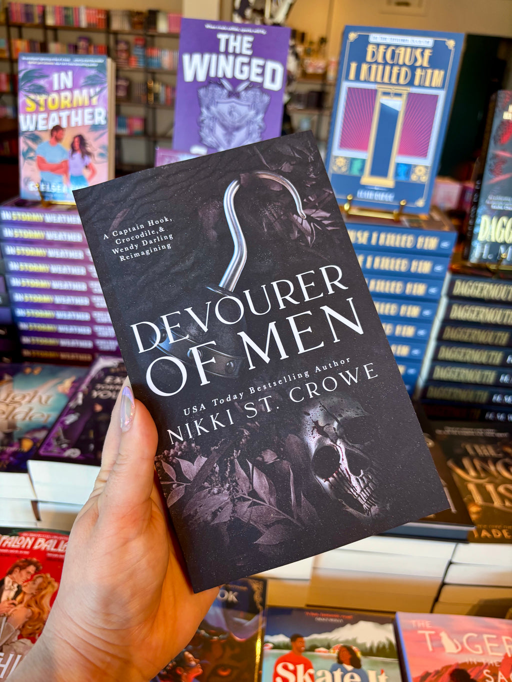 A hand holds the book 'Devourer of Men' by Nikki St. Crowe in a bookstore, with other books visible in the background.