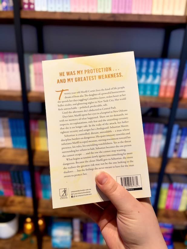 A hand holding the back of a copy of 'Drawn Together' by Mercedes Ron with a white background, gold accents, and black text.