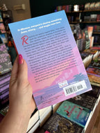 A hand with pink nail polish holding the back of a copy of 'Formula: He's the One' featuring a cityscape and text.