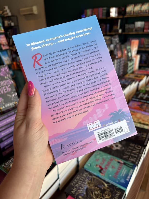 A hand with pink nail polish holding the back of a copy of 'Formula: He's the One' featuring a cityscape and text.