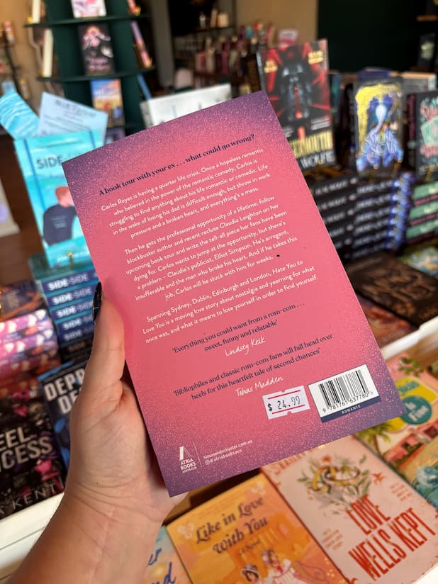 A hand holds the back cover of 'Hate You to Love You' by Joshua Hortinela with white font on a pink background for the blurb.