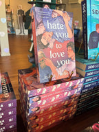 A stack of 'Hate You to Love You' by Joshua Hortinela books with alternating spine and sprayed edges facing out. The cover features an illustration of two men lying down and digitally sprayed edges featuring open books and headphones.