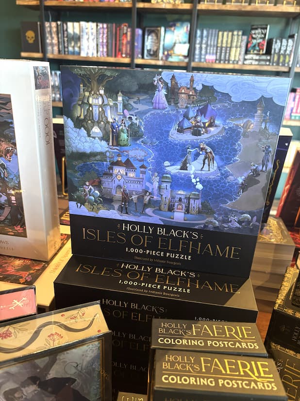 A stack 1000 piece puzzle boxes featuring an illustration of a fantasy landscape with buildings and people, titled 'Holly Black's Isles of Elfhame'.