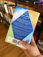 A hand holding the back of a copy of 'Ice Planet Barbarians' by Ruby Dixon, featuring a colourful triangles and a large blue diamond in the centre with white text.