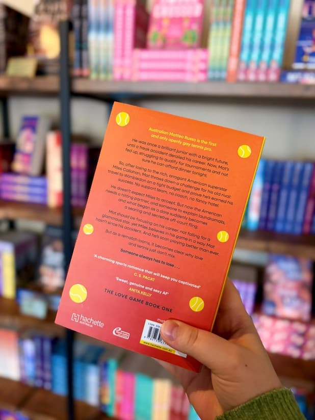 A hand holds the back of the book 'In Your Court' by Kit Haley, featuring a bright orange cover with black and yellow text.