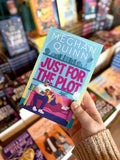 A hand holding a copy of for 'Just for the Plot' by Meghan Quinn, featuring a colorful illustration of a man and woman sitting on a pink couch in a living room, with a woman reclined in his lap. They're reading the same book. 
