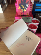 A hand holds an open copy of 'Kill to Love' by Penny Sunday, with a red signature under the title page.