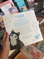 A hand holds the back cover for the Lights Out Official colouring book showing a cat in the bottom left corner and the outline of roses framing blue and black 