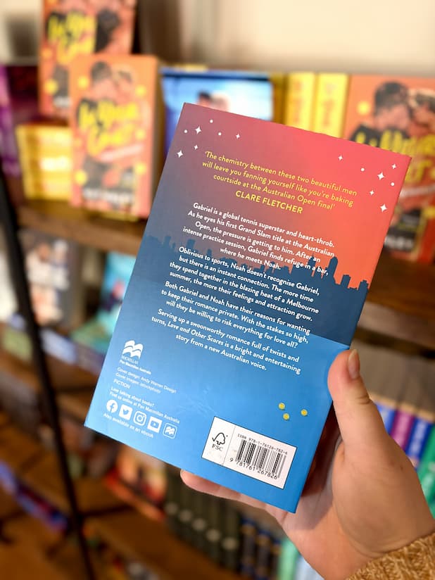 A hand holding the back of a copy of 'Love and Other Scores' by Abra Pressler, featuring yellow and white text against a city skyline.