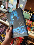 A hand holds the paperback book 'Loving the Wicked' by Becca Johnpee in a bookstore, with other books visible on the shelves in the background.
