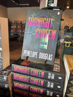 A stack of paperback copies of 'Midnight Curfew' by Penelope Douglas, featuring a dark gothic stone archway in the rain with large gradient title text in pink, orange, and yellow.