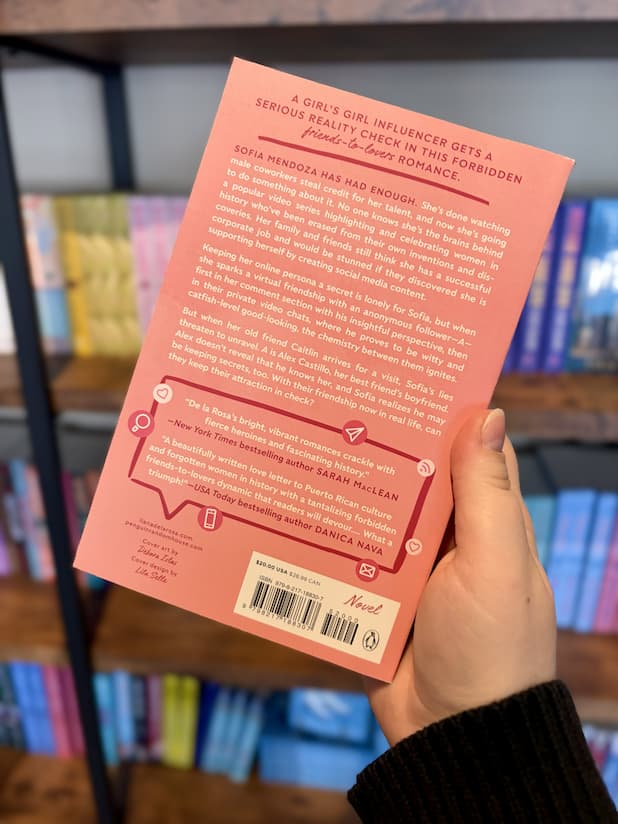 A hand holding the back of a copy of 'Mutual Discord' by Liana de la Rosa, featuring a peach background with red and white text.