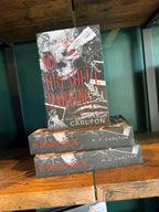 A stack of the book 'My Dreadful Darling' with keys, feathers, and text on a dark background on a wooden bookshelf with a green background.