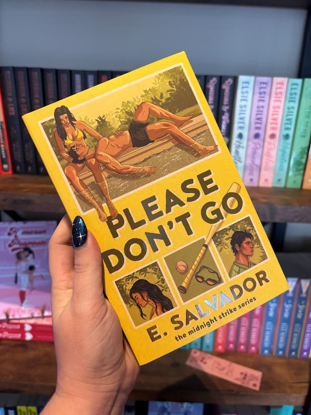 A hand holds the book cover for 'Please Don't Go' by E. Salvador, featuring a retro-style illustrated design with a yellow background, green title text, and vintage photographs of the main characters and baseball elements, in front of a blurry bookshelf full of books.