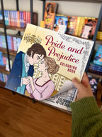 A hand holding a copy of 'Pride and Prejudice Colouring Book' featuring an illustrated Regency couple in an elegant room, with decorative floral borders.