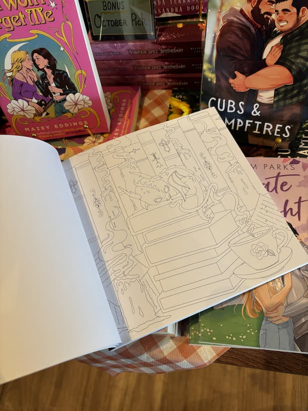 An open copy of 'Romantasy Coloring Book' with an illustration of a baby dragon sleeping atop a stack of books.