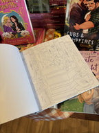 An open copy of 'Romantasy Coloring Book' with an illustration of a baby dragon sleeping atop a stack of books.