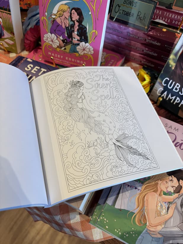 An open copy of 'Romantasy Coloring Book' with an illustration of a mermaid.
