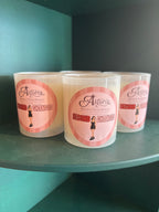 Three white soy candles in clear glass jars with pink and white labels reading 'Astoria Second Chances', displayed on a dark teal shelf.