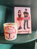 A white jar candle and a pink book titled 'Second Chances' by Summer-Lee Deaves are displayed on a dark teal shelf.