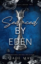 Book cover of 'Seduced by Eden' by Jade May. The cover is dark blue with a silver chess piece in the centre and grey roses on the top and bottom of the cover.