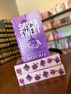 A stack of 'Silver Sweet' by Krista & Becca Ritchie with a purple background and rose design, and matching sprayed edges with purple roses.